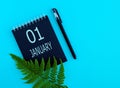 January 1th. Day 1 of month, Calendar date. Black notepad sheet, pen, fern twig, on a blue background