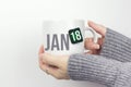 January 18th. Day 18 of month, Calendar date. Closeup of female hands in grey sweater holding cup of tea with month and calendar