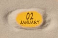 January 2. 2th day of the month, calendar date. Hole in sand. Yellow background is visible through hole