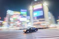 A taxi zooms pass the busy street of Shibuya crossing, Japan