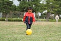 Japanese boy kicking a yellow ball on the grass Royalty Free Stock Photo