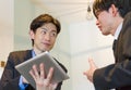 Japanese business person talking with colleague, showing data with tablet device