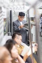 Japanese businessman taking ride to work in morning, standing inside public transport and reading newspaper.