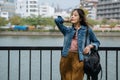 Japanese businesswoman relaxing near the clean river with winds blowing hair on holiday. young office lady rest relying on