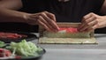 Japanese chef prepares sushi rolls with salmon and avocado. Cook hands making Japanese sushi roll on the bamboo mat