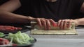 Japanese chef prepares sushi rolls with salmon and avocado. Cook hands making Japanese sushi roll on the bamboo mat