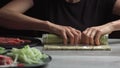 Japanese chef prepares sushi rolls with salmon and avocado. Cook hands making Japanese sushi roll on the bamboo mat