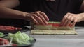 Japanese chef prepares sushi rolls with salmon and avocado. Cook hands making Japanese sushi roll on the bamboo mat