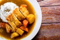 Japanese curry with rice, black sesame, carrot, potato and deep fries chicken in white dish on wooden table