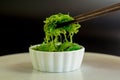 Japanese food concept. Fresh seaweed salad with sesame seeds in white bowl with chopstick on black background Royalty Free Stock Photo