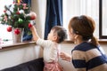 1-year-old girl and mother decorating Christmas tree