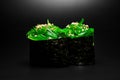 Japanese gunkan sushi with chukka and sesame seeds wrapped in nori seaweed on dark background.