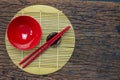 Japanese kitchenware set of red chopsticks, bowls and cup on bamboo mat and wooden table background Royalty Free Stock Photo