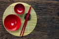 Japanese kitchenware set of red chopsticks, bowls and cup on bamboo mat and wooden table background