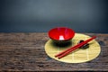 Japanese kitchenware set of red chopsticks, bowls and cup on bamboo mat on wooden table