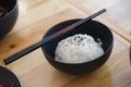 Japanese rice with black sesami on top in the black bowl and chopsticks on the wood table