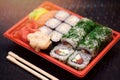 Japanese sushi in red plastic container for carrying food on black. Roll made of crab meat, avocado, cucumber inside and Royalty Free Stock Photo