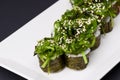 Japanese sushi with rice and fish and seaweed salad on top. Served on a white plate over black background Royalty Free Stock Photo