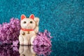 Japanese symbol of good luck maneki neko cat framed by lilac flowers on a blue bokeh background