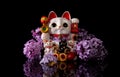 Japanese symbol of good luck maneki neko cat framed by pink lilac flowers on a black background