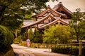 Japanese temple building with four roofs in the gardens of Kiyomizu Shrine with a geisha walking on a quiet pathway