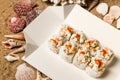 Japanese Volcano Sushi Roll pieces with raw scallop and flying fish roe on carton delivery takeaway box. sand background with shel Royalty Free Stock Photo