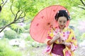 Traditional Asian Japanese beautiful Geisha woman wears kimono bride with a red umbrella in a graden Royalty Free Stock Photo