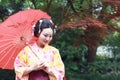 Traditional Asian Japanese beautiful Geisha woman wears kimono hold a umbrella on hand under a tree in a summer graden Royalty Free Stock Photo