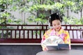 Traditional Asian Japanese beautiful Geisha woman bride wears kimono hold a fan reading book in a summer nature Royalty Free Stock Photo