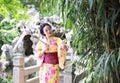 Traditional Asian Japanese beautiful Geisha woman wears kimono hold red white umbrella by bamboo in a summer spring outdorr garden Royalty Free Stock Photo