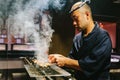 Japanese Yakitori Chef is grilling chicken marinated with ginger, garlic and soy sauce with a lot of smoke