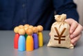 A businessman holds a japanese yen money bag near a group of people figurines.