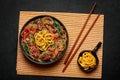 Japchae in black bowl on dark slate table top. Korean cuisine glass chapchae noodles dish with vegetables and meat