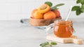 A jar of apricot jam with a spoon inside, ripe apricots in a plate and a branch with green leaves. Fruit preservation. Royalty Free Stock Photo