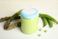 Jar with baby food, fresh pea pods and asparagus on white table Royalty Free Stock Photo