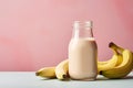 Jar with banana milkshake or smoothie in front of pastel pink colored background