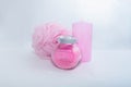 A Jar of bath salt, a sponge for bath and a candle are stand nearby. Light pink objects on a white background. The