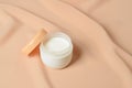 A jar of cream for caring for delicate skin on a wavy beige background made of chiffon