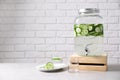 Jar dispenser of fresh cucumber water and glasses on table against brick wall. Royalty Free Stock Photo