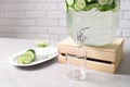 Jar dispenser of fresh cucumber water and glasses on table against brick wall. Royalty Free Stock Photo