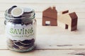 Jar with full of coins inside with wooden house model background. Home finance concept