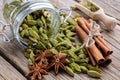 Jar of green cardamom pods. Cinnamon sticks, cardamom seeds, wooden scoop and anise stars on table Royalty Free Stock Photo
