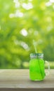 Jar with green ice drink and straw on wooden table over green tr Royalty Free Stock Photo