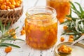 Jar of healthy sea buckthorn jam. Basket of ripe sea buckthorn berries on background. A spoonful of jam in the foreground