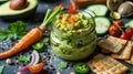 A jar of homemade guacamole surrounded by sliced vegetables and whole grain crackers illustrating the versatility of