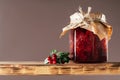 Jar of lingonberry and pear jam with craft paper on lid on wooden shelf next to fresh lingonberries on brown background