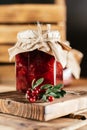Jar of homemade lingonberry and pear jam with craft paper on lid on wooden table next to fresh lingonberries. Vertical