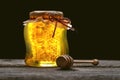 Jar of honey with honeycomb with wooden dipper on wooden table