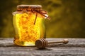 Jar of honey with honeycomb with wooden dipper on wooden table