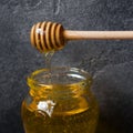 A jar of liquid honey from Linden flowers and a stick with honey on a dark background